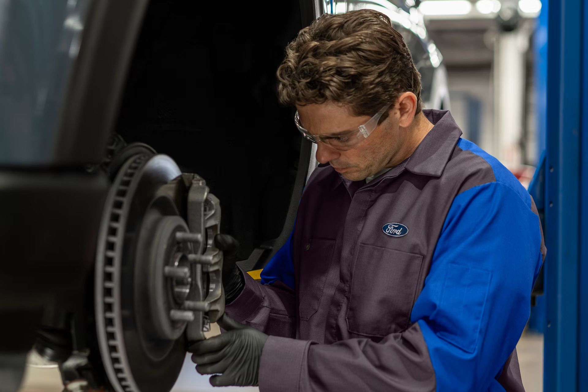 Ford technician inspecting a brake rotor and caliper on a vehicle raised on a lift